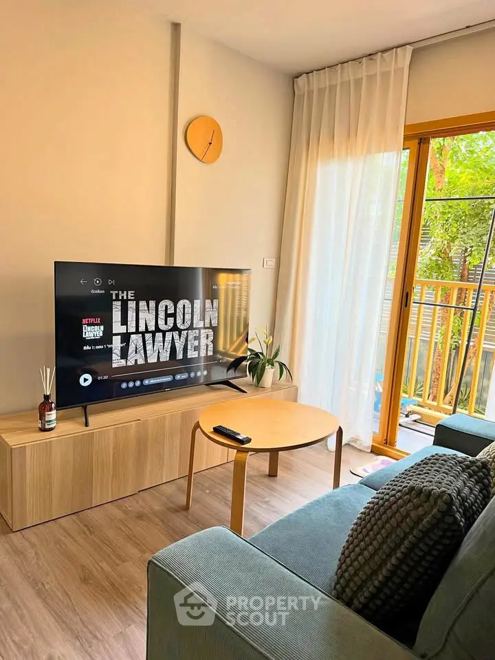 Modern living room with stylish decor, featuring a large TV and cozy seating area, overlooking a lush balcony view.