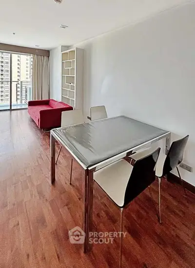 Modern living room with sleek dining area and red sofa, featuring floor-to-ceiling windows and wooden flooring.