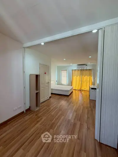 Spacious bedroom with wooden flooring and natural light