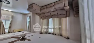 Spacious living room with large windows and elegant curtains, featuring a ceiling fan and comfortable seating.