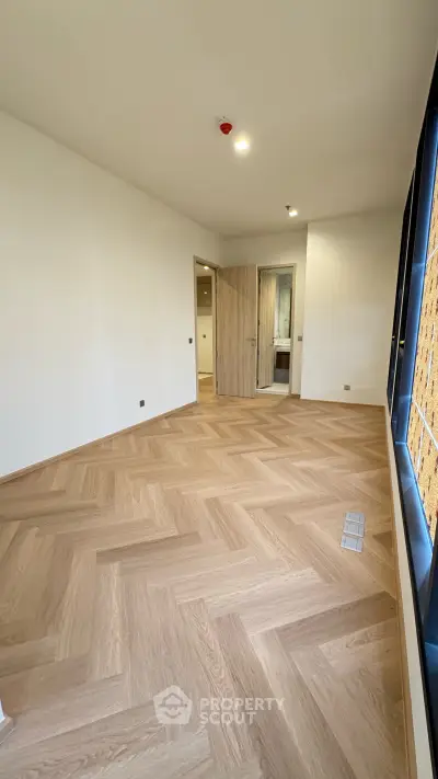 Spacious empty room with elegant wooden flooring and large window, perfect for customization.
