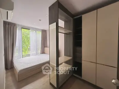 Modern bedroom with large window and built-in wardrobe, offering a serene view of lush greenery.