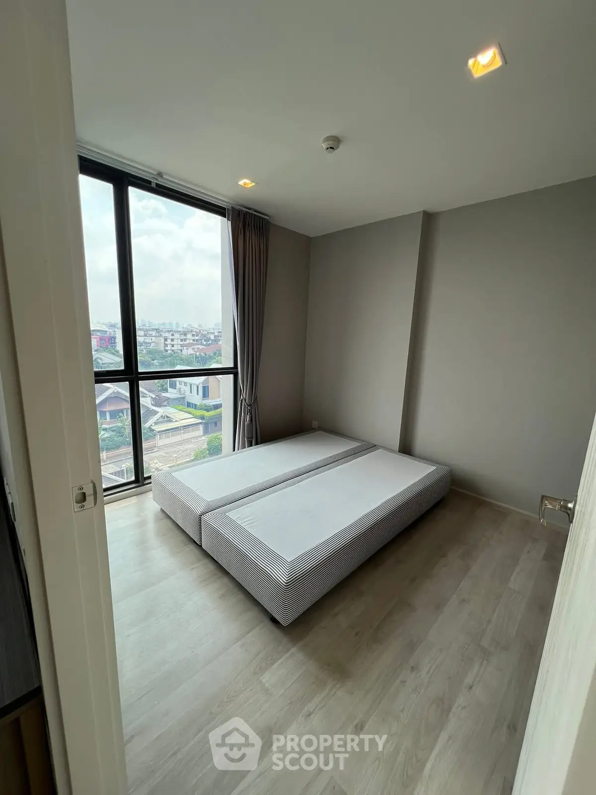 Modern bedroom with large window offering city views, featuring minimalist design and ample natural light.