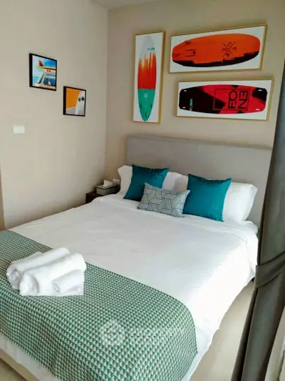 Modern bedroom with stylish decor and surfboard art, featuring a cozy bed and vibrant pillows.