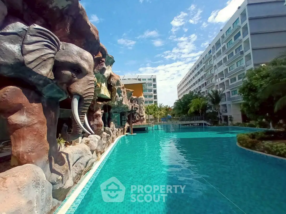 Luxurious poolside view with unique elephant sculpture and modern apartment buildings under a clear blue sky.