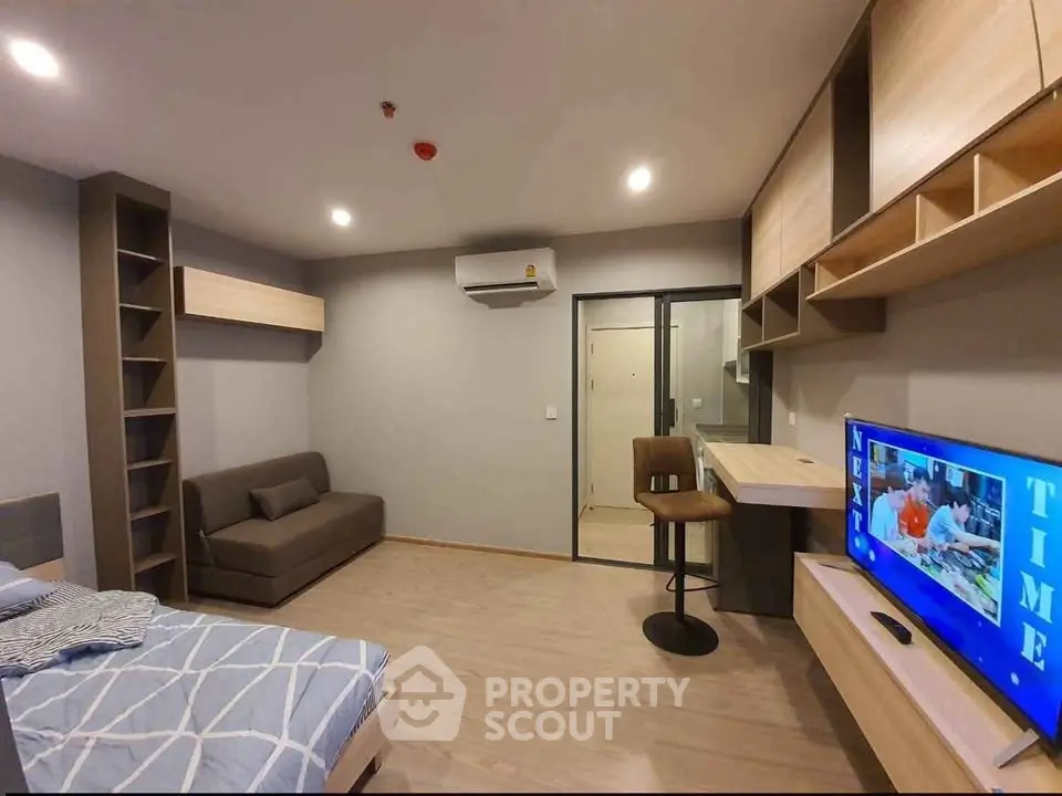 Modern studio apartment with stylish furniture and open layout, featuring a cozy bed, sofa, and wall-mounted TV.