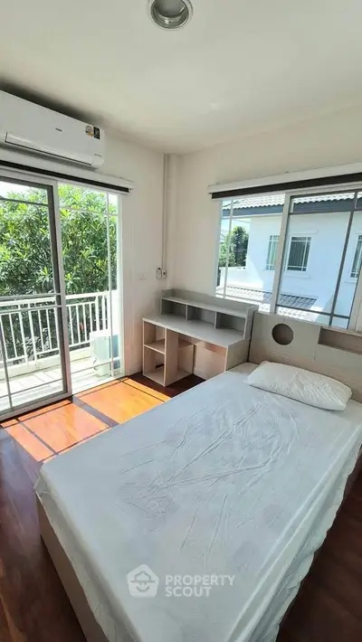 Bright bedroom with large windows and balcony access, featuring a single bed and modern air conditioning unit.