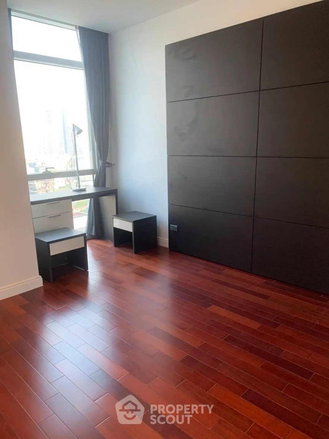 Spacious room with hardwood floors and large window offering city views, ideal for modern living.