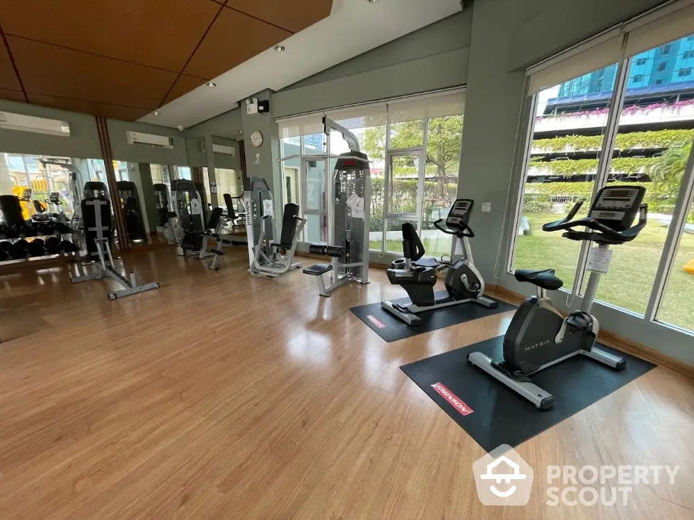 Modern gym with exercise equipment and large windows overlooking greenery