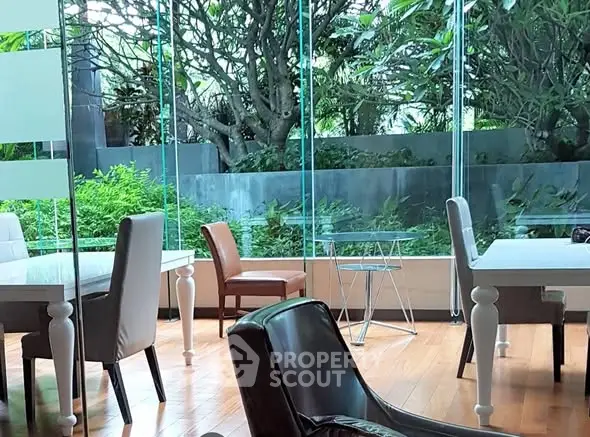 Modern living room with large glass windows and lush garden view, featuring elegant furniture.