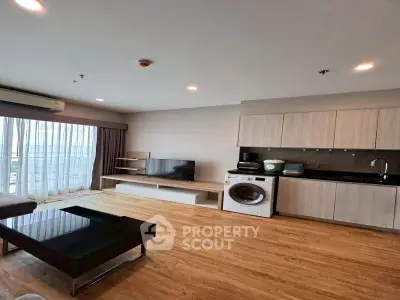 Modern living room with open kitchen, featuring wooden floors and natural light.