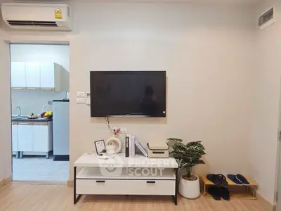 Modern living room with wall-mounted TV and stylish decor, adjacent to a compact kitchen area.