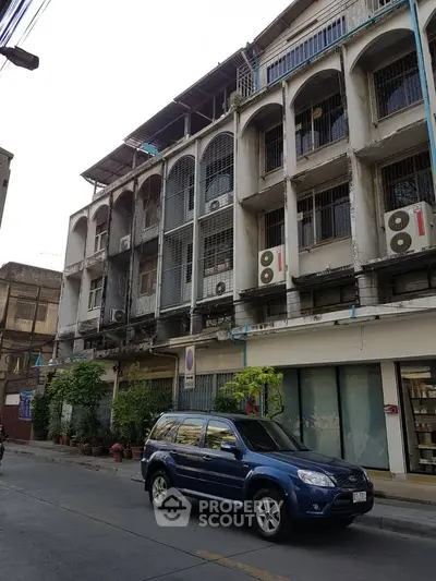 Urban street view of a multi-story building with balconies and parked car.