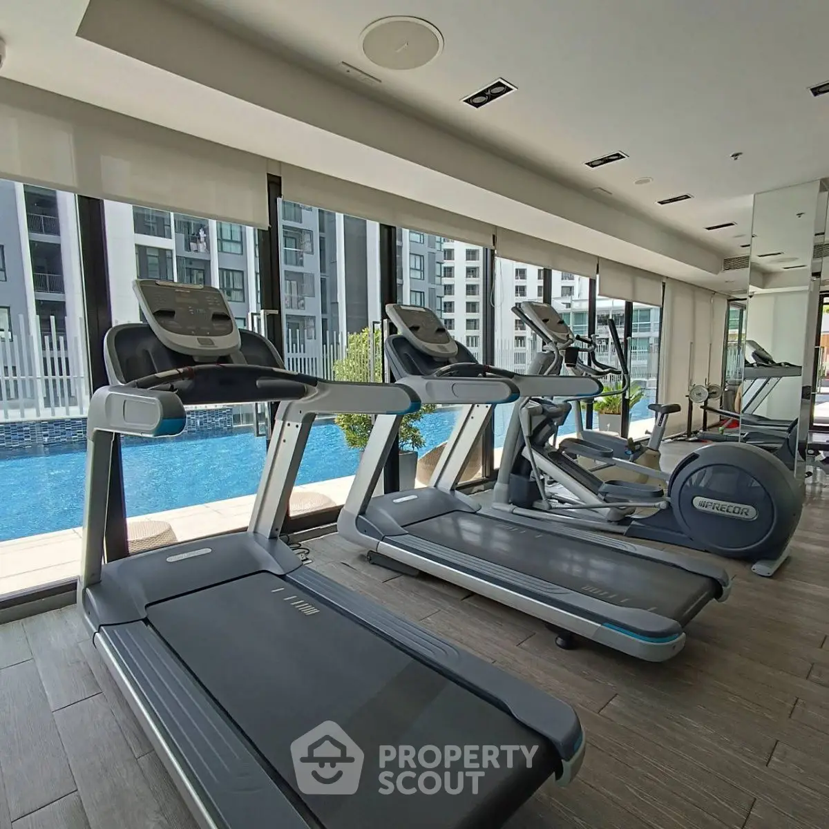 Modern gym with treadmills overlooking a pool in a luxury apartment complex.