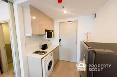 Modern compact kitchen with washing machine and sleek appliances in a cozy apartment.