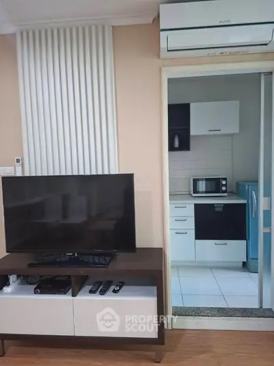 Modern living room with TV and view into compact kitchen with appliances.