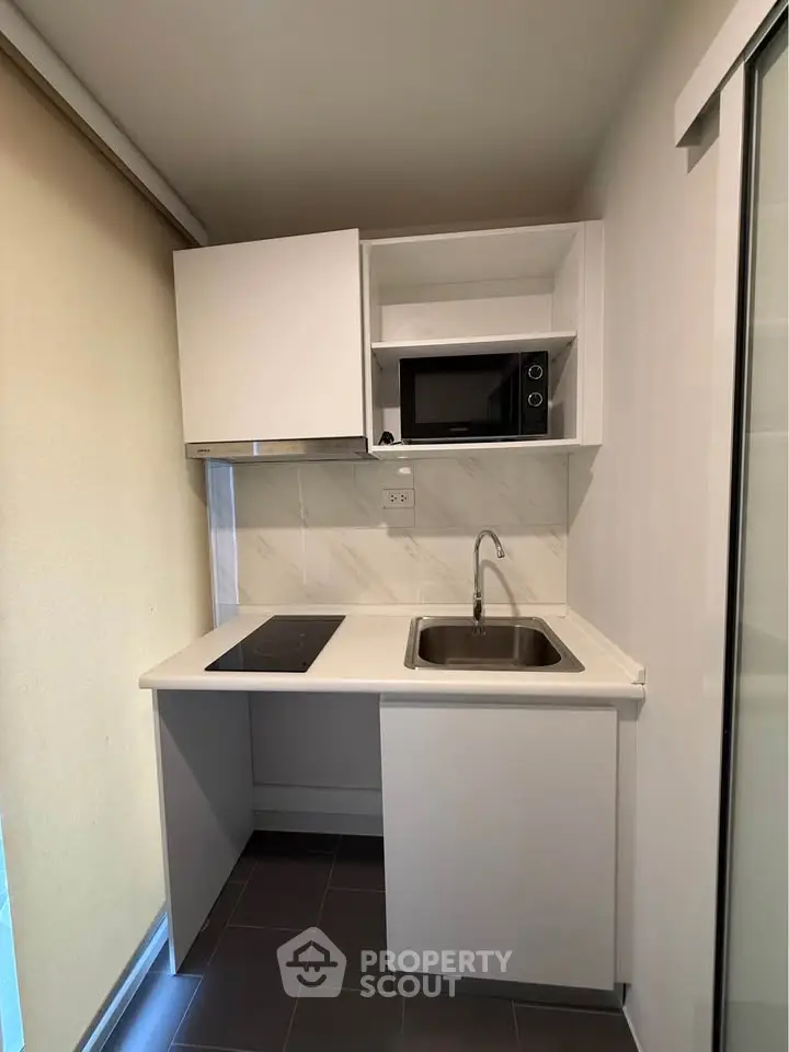 Compact modern kitchen with sleek white cabinets and built-in microwave, ideal for small apartments.