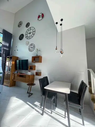 Modern living room with high ceiling and stylish decor featuring wall clocks and pendant lights.