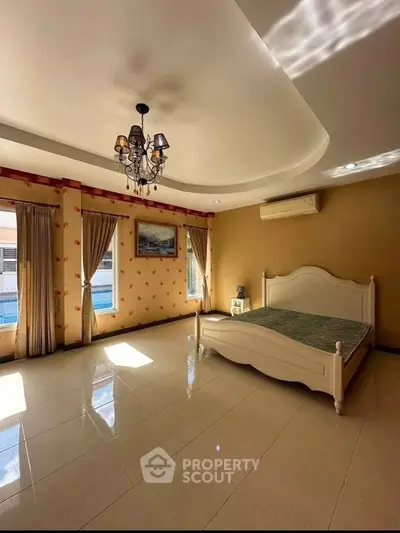 Spacious bedroom with elegant chandelier and large windows offering natural light.