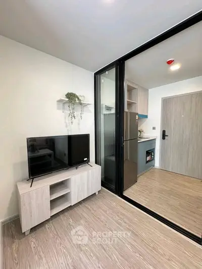 Modern living room with TV and sliding glass door to kitchen in stylish apartment.
