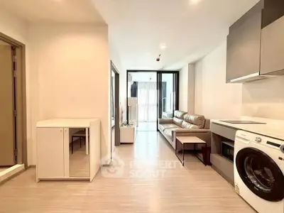 Modern open-plan living room with kitchen featuring washing machine and sleek furniture.