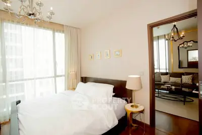 Elegant bedroom with modern decor and large window, adjacent to cozy living room.