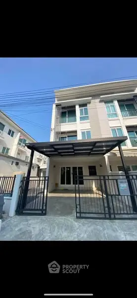 Modern townhouse exterior with gated entrance and carport in urban setting.