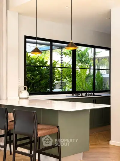 Modern kitchen with open layout, featuring sleek countertops and large windows overlooking lush greenery.