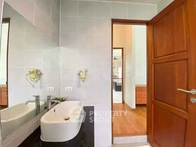 Modern bathroom with sleek sink and wooden door, leading to a bright hallway.