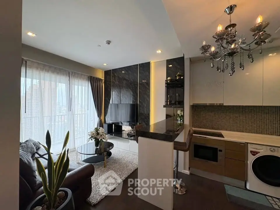 Luxurious modern living room with open kitchen, featuring elegant chandelier and stylish decor.