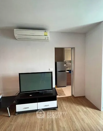 Modern living room with TV and air conditioning, adjacent to a kitchen with a fridge.