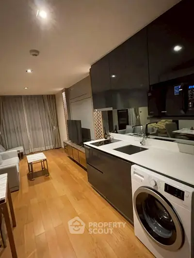 Modern living room with sleek kitchen and washing machine, featuring elegant wood flooring and stylish decor.