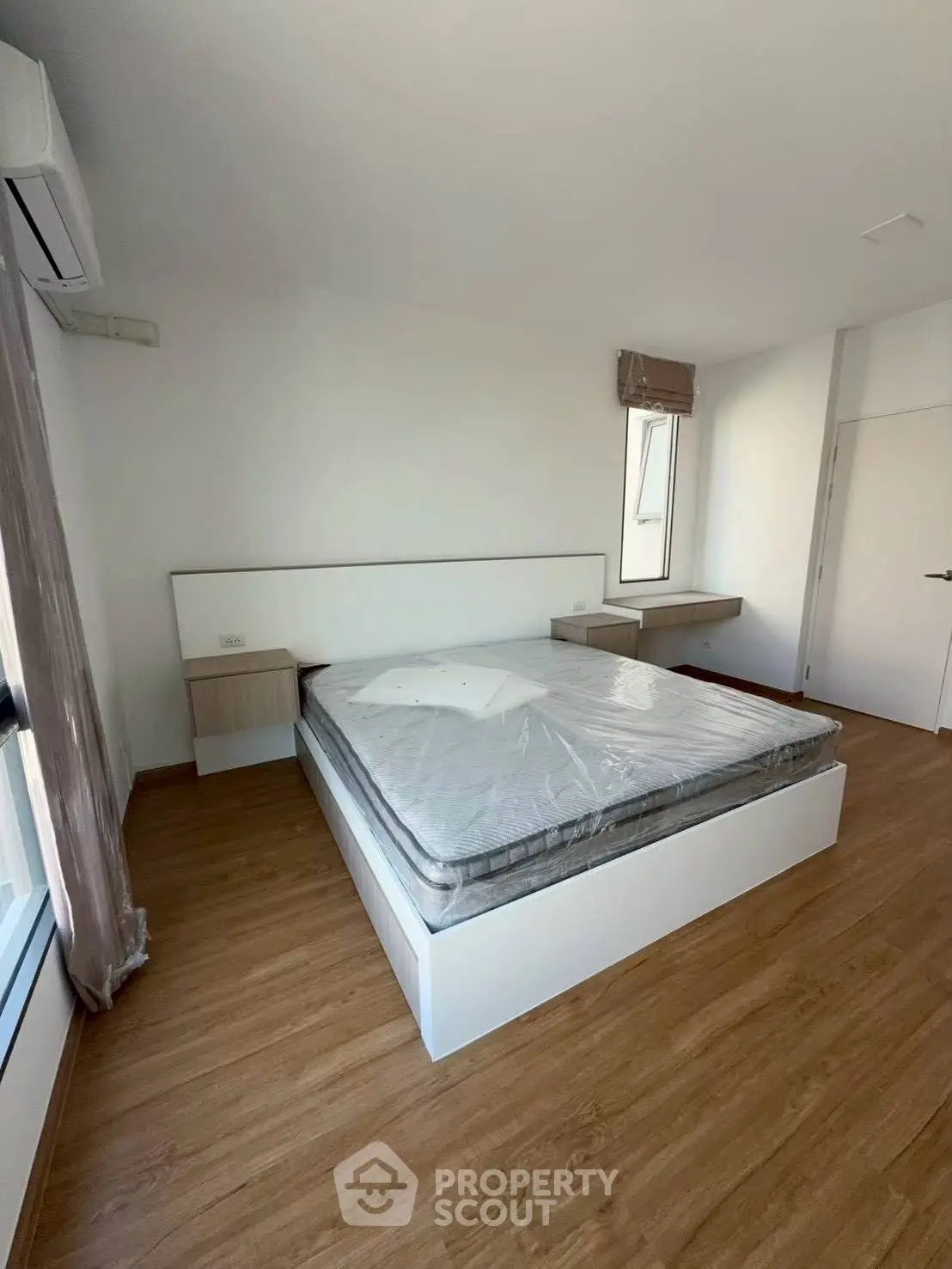 Spacious bedroom with modern design and natural light, featuring a large bed and wooden flooring.