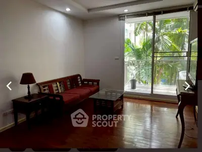 Spacious living room with wooden flooring and large glass doors opening to a lush green view.