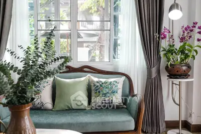 Charming living room with elegant sofa, lush plants, and natural light through large window.
