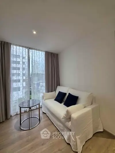 Cozy living room with white sofa and modern round table, featuring floor-to-ceiling windows and elegant curtains.