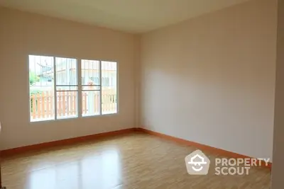 Spacious empty room with wooden flooring and large window for natural light.