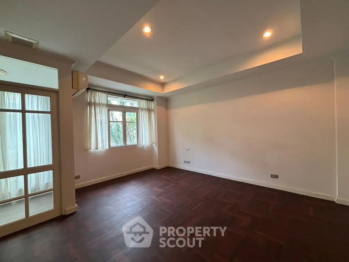 Spacious empty living room with elegant parquet flooring and large windows for natural light.