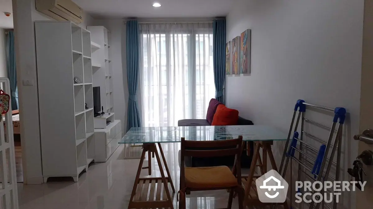 Spacious and well-lit living area with modern furnishings, large windows draped with stylish curtains, and a cozy dining set, perfect for urban living.