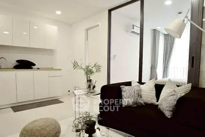 Modern living room with sleek kitchen in open layout, featuring stylish decor and natural light.