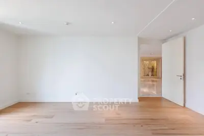 Spacious empty room with wooden flooring and open door leading to another area.
