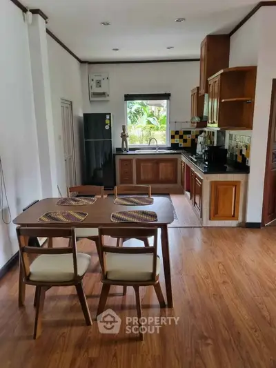 Charming kitchen with wooden cabinets and dining area, featuring a window view of lush greenery.
