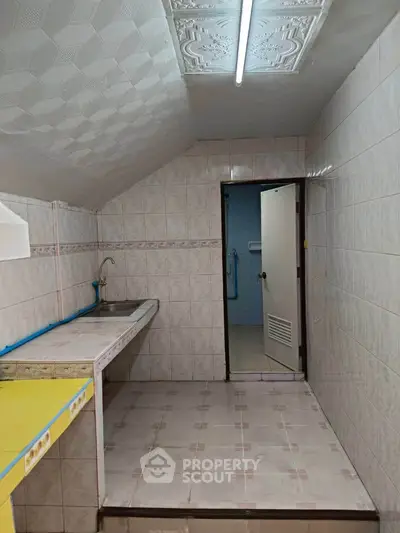 Compact kitchen with tiled walls and ceiling, featuring a single sink and fluorescent lighting.
