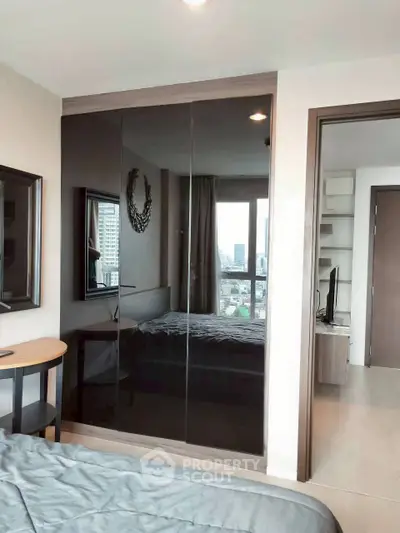 Modern bedroom with city view and sleek mirrored wardrobe in a stylish apartment.