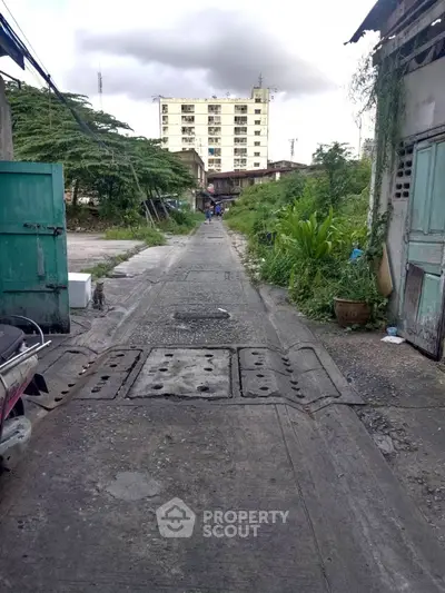 Urban alleyway leading to a residential building with lush greenery on the sides.