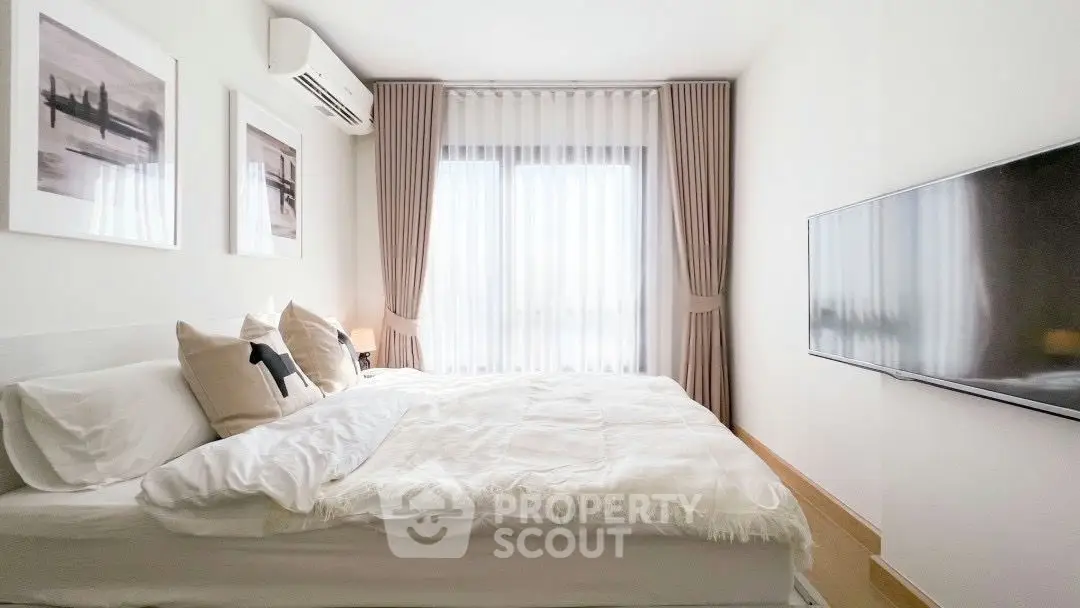 Modern bedroom with cozy bed, wall-mounted TV, and elegant curtains in a bright apartment.