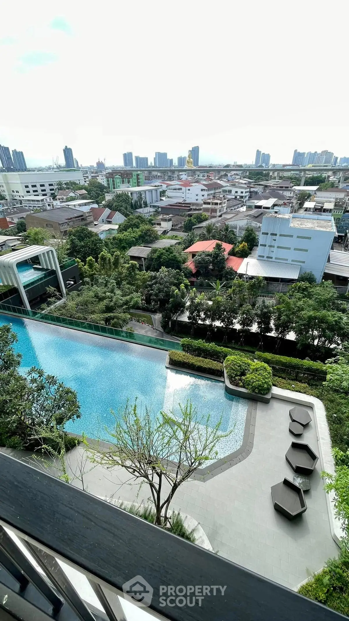 Stunning cityscape view from a high-rise balcony overlooking a luxurious pool and lush greenery.