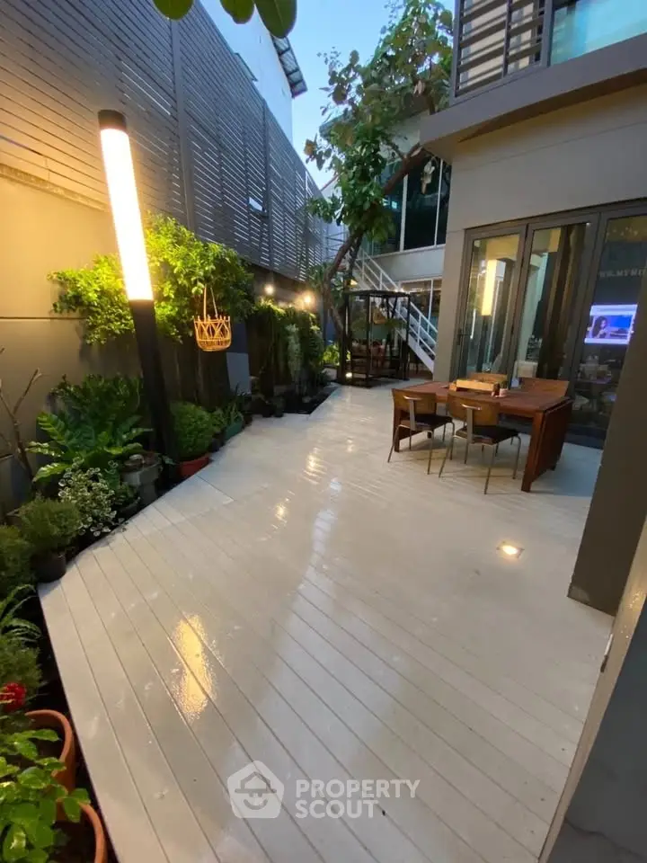 Charming outdoor patio with modern lighting and lush greenery, perfect for relaxation and entertaining.