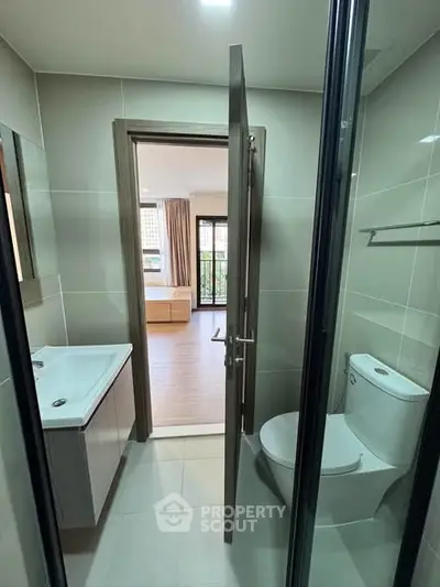 Modern bathroom with sleek fixtures and view into a bright bedroom with large windows.