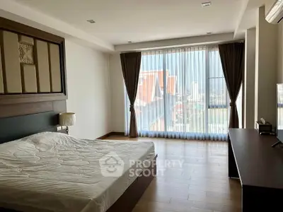 Spacious bedroom with large windows and city view, featuring elegant wooden flooring.